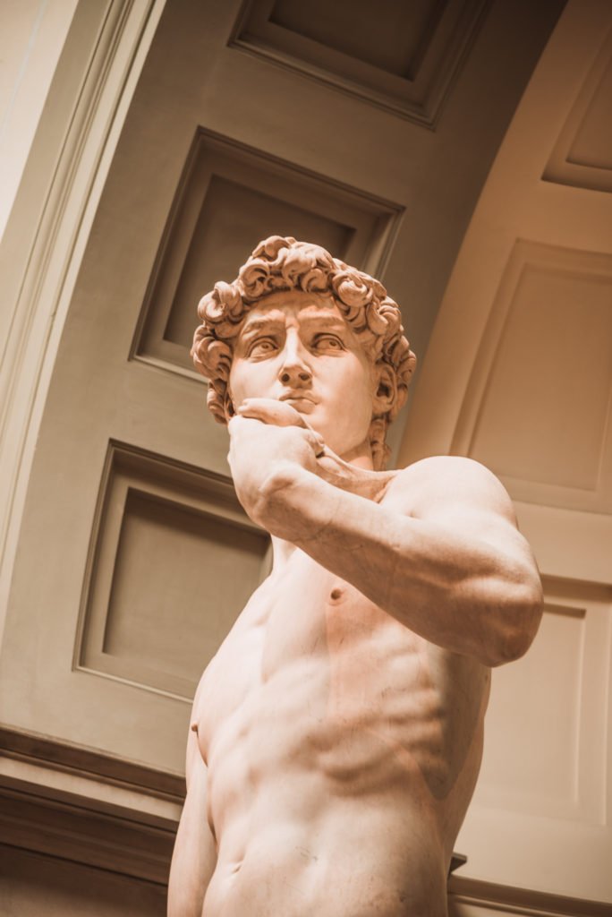 The Perfect 3 Day Florence Itinerary (From an Italy Travel Expert) 13 Michelangelo's David, a tall white marble statue of a nude young man standing in a relaxed pose with a sling over his shoulder, displayed in an arched alcove at the Accademia Gallery in Florence