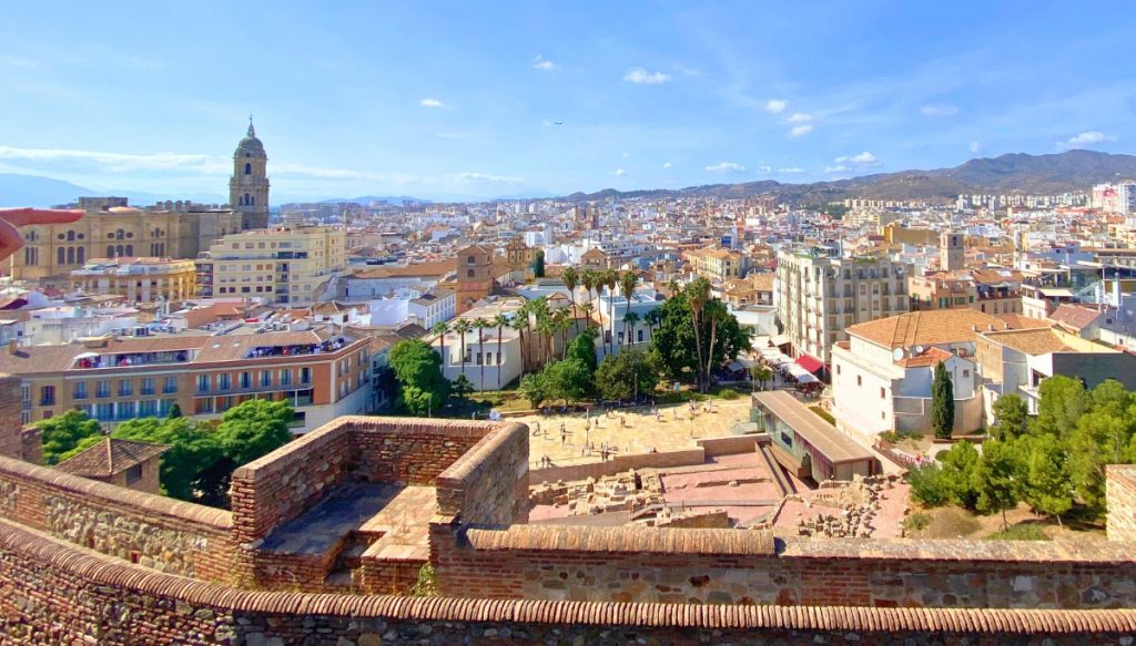 34 Incredible Weekend Trips From Barcelona 21 Panoramic view of Málaga, Spain, showcasing the city's diverse architecture with historical buildings in the foreground and modern cityscape in the distance, under a clear blue sky