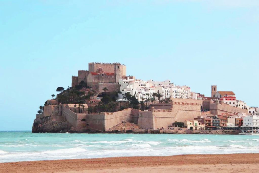 34 Incredible Weekend Trips From Barcelona 29 View of Peñíscola, Spain, with its iconic castle perched on a hill surrounded by white-washed houses, overlooking the sandy beach and the azure waters of the Mediterranean Sea.