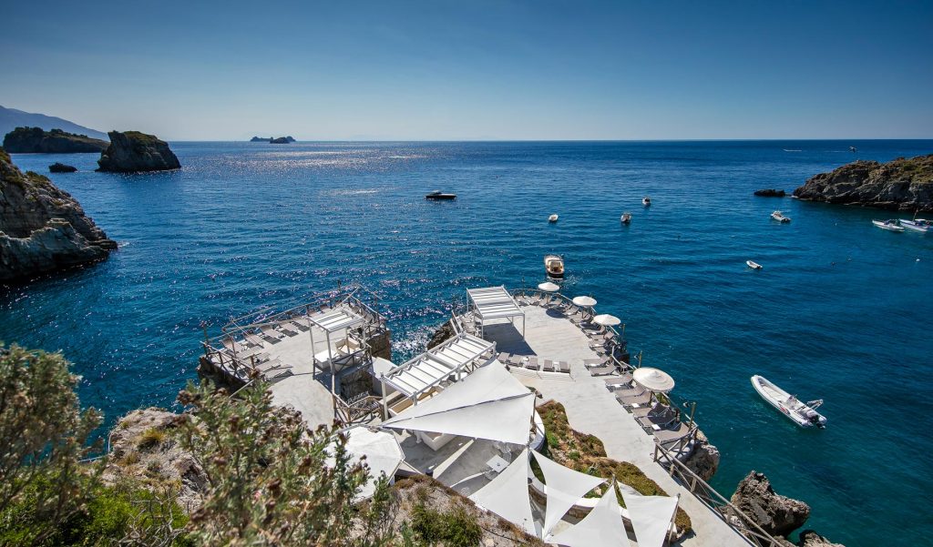 20 Best Amalfi Coast Beach Clubs 34 A breathtaking view of Conca del Sogno, with white sunbeds and umbrellas on a rocky outcrop overlooking the sparkling blue waters of the Mediterranean Sea, boats anchored in the calm bay