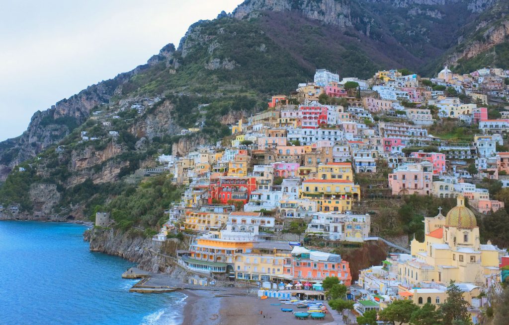 The Most Luxurious 5 Day Amalfi Coast Itinerary 10 A stunning view of Positano's colorful hillside homes cascading down towards the blue waters of the Amalfi Coast, surrounded by rugged cliffs and lush greenery.