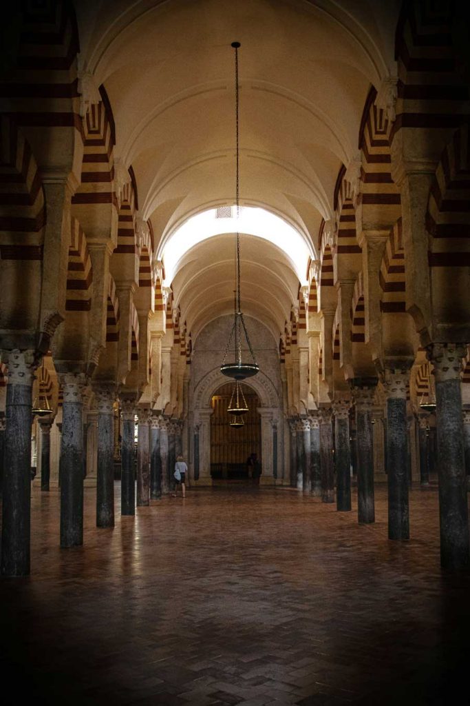 3 Most Amazing Days In Seville, Spain 30 Expansive hallway of the Mezquita-Catedral in Córdoba showcasing rows of Moorish arches with alternating red and white stripes supported by tall marble columns under dim lighting.