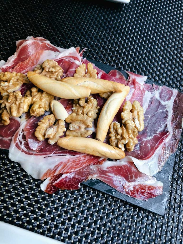 3 Most Amazing Days In Seville, Spain 14 A slate plate topped with thin slices of jamón ibérico, walnuts, and crunchy breadsticks sits on a dark woven placemat.