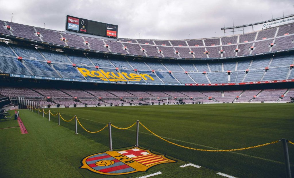 3 Days in Barcelona: The Perfect Itinerary for First-Time Visitors 45 A wide-angle view of FC Barcelona's iconic Camp Nou stadium, featuring its vast, empty blue and red seats, with "Rakuten" displayed in yellow letters. The lush green field is roped off with yellow chains, and the FC Barcelona crest is painted on the ground in the foreground.