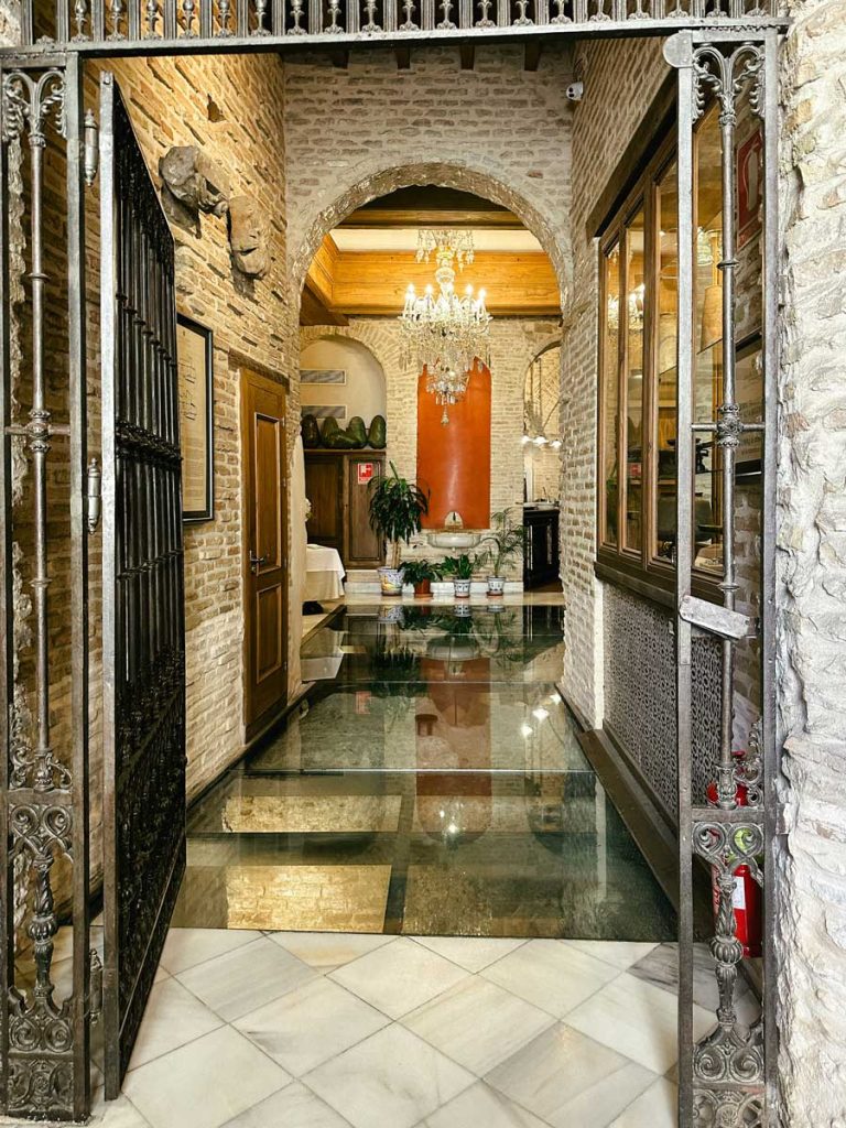 3 Most Amazing Days In Seville, Spain 25 Interior of a charming Italian restaurant in Seville with a chandelier, exposed brick walls, arched entrance, and glass floor revealing a stone cellar below.