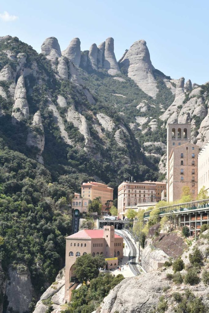 3 Days in Barcelona: The Perfect Itinerary for First-Time Visitors 46 A close-up of the Santa Maria de Montserrat Abbey, nestled among the rugged Montserrat mountains. The historic stone buildings contrast with the dramatic rock formations and green foliage surrounding them.