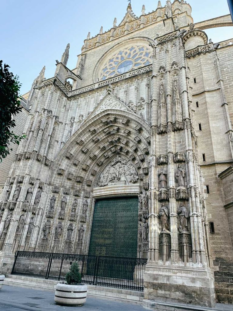 3 Most Amazing Days In Seville, Spain 22 Grand Gothic façade of Seville Cathedral with a large rose window, ornate stone carvings, and towering spires captured under a clear sky.