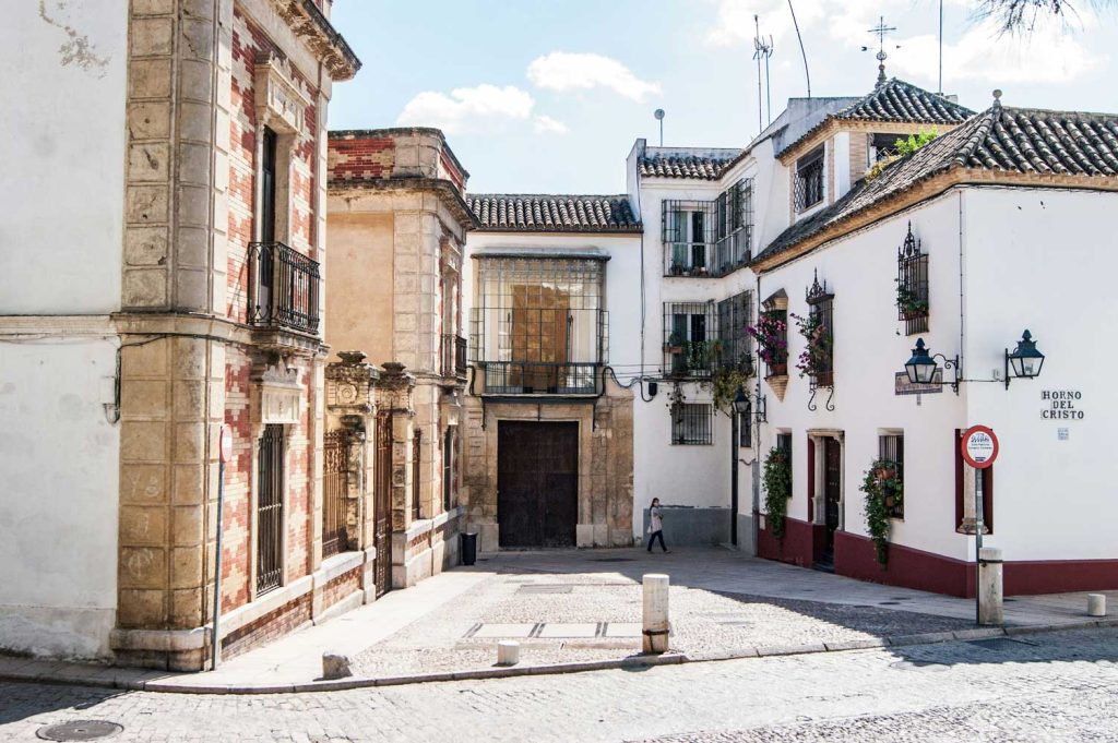 3 Most Amazing Days In Seville, Spain 29 Quiet corner in Córdoba’s old town with cobbled streets, a mix of white and stone buildings, balconies with iron railings, and flowering plants under a clear afternoon sky.