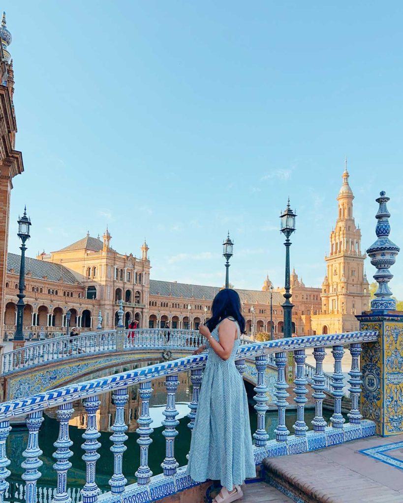 3 Most Amazing Days In Seville, Spain 12 Woman looks out over the tiled bridge at Plaza de España with its decorative ceramic railing, watching the golden architecture reflect in the water below.