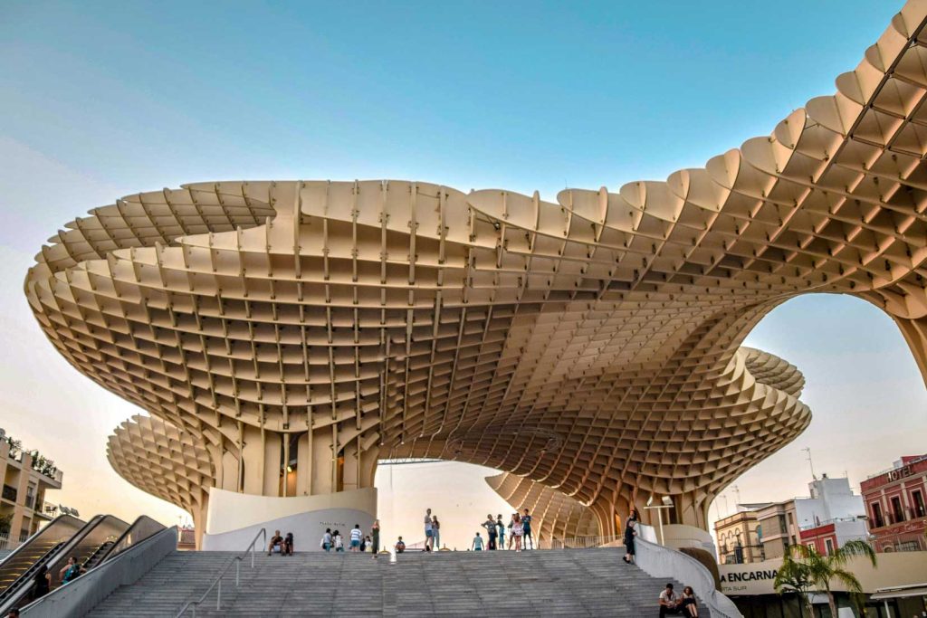 3 Most Amazing Days In Seville, Spain 13 Wide-angle view of the Metropol Parasol in Seville, a massive wooden architectural structure with a waffle-like pattern, as visitors walk and sit beneath it on a sunny day.