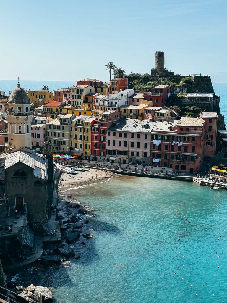 15 Amazing Day Trips From Florence, Italy 25 An overhead view of Vernazza’s beach and harbor surrounded by colorful pastel buildings and a medieval tower perched on a cliff.