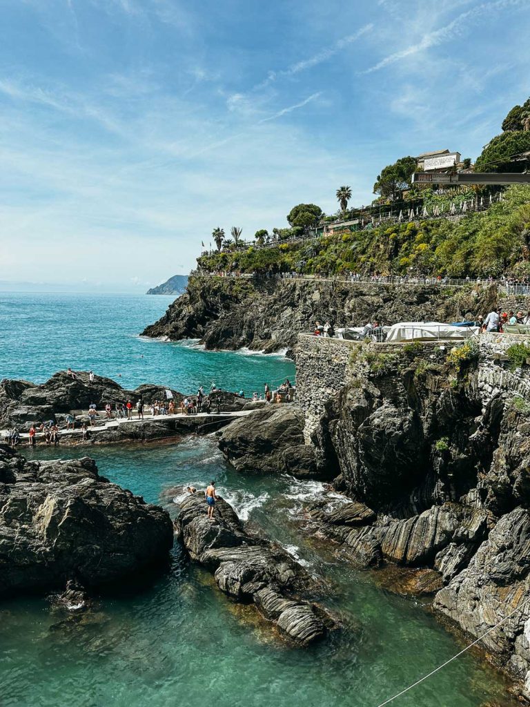 Portofino Or Cinque Terre: Which Is Better? 28 Tourists walk along a rocky coastal path above turquoise waters and jagged cliffs in the seaside town of Manarola, Cinque Terre.