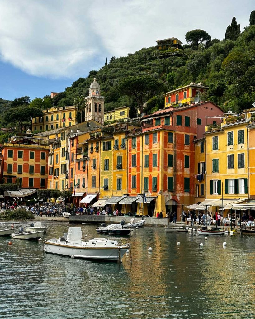 Portofino Or Cinque Terre: Which Is Better? 11 Boats bob in the harbor in front of a row of tall, narrow Portofino buildings painted in rich shades of yellow, red, and orange.