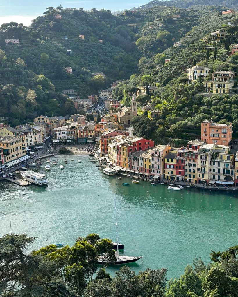 20 Best European Summer Destinations To Visit This Year 14 An elevated view of Portofino’s harbor shows pastel buildings, boats, and lush green hills wrapping around turquoise water.