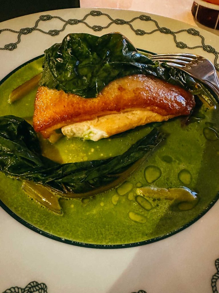 Portofino Or Cinque Terre: Which Is Better? 25 A seared fillet of fish rests on creamy sauce with wilted greens, served on an elegant plate with a fork placed on the side.