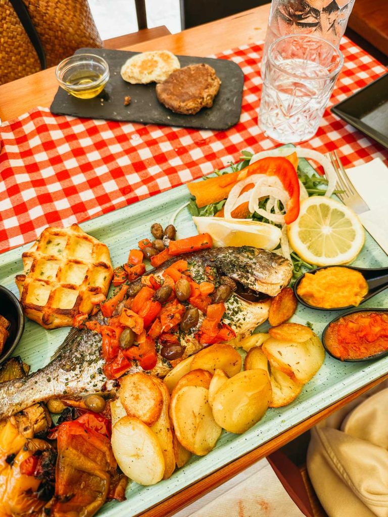 Portofino Or Cinque Terre: Which Is Better? 26 A Mediterranean seafood platter with grilled whole fish, roasted potatoes, grilled vegetables, salad, and small sides served on a green ceramic tray with bread on the side.