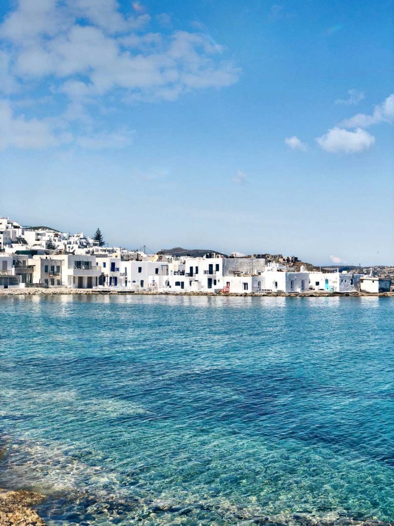 20 Best European Summer Destinations To Visit This Year 38 Whitewashed buildings line a calm turquoise harbor under a bright blue sky with soft clouds. The coastal village scene captures the charm of European summer destinations along the Mediterranean.