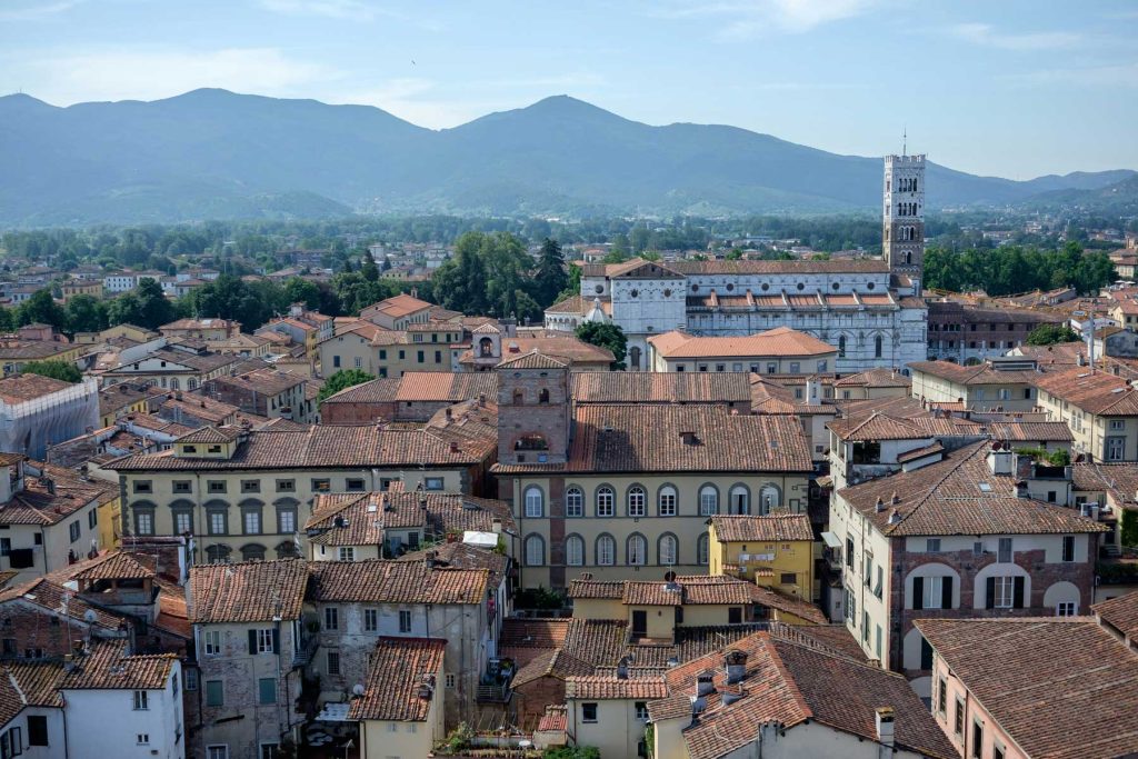 15 Amazing Day Trips From Florence, Italy 21 Rooftop view over a historic Italian city with terracotta buildings in the foreground, a white church and tall bell tower rising near the center, and blue mountains in the distance. The layered cityscape works well for how to plan travel abroad during uncertainty because it suggests an urban destination where route changes and flexible itineraries can be important.