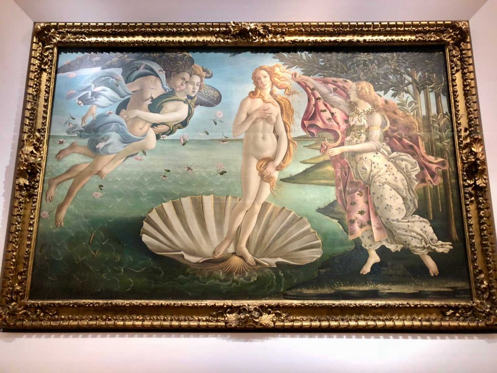 The Perfect 3 Day Florence Itinerary (From an Italy Travel Expert) 16 Botticelli’s The Birth of Venus displayed in an ornate gold frame inside the Uffizi Gallery in Florence. Venus stands on a shell in the center of the painting with figures flying and reaching toward her on either side.