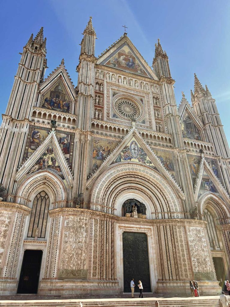15 Amazing Day Trips From Florence, Italy 30 Ornate cathedral facade with mosaics. Sculpted arches and a large rose window rise above people standing near the entrance.